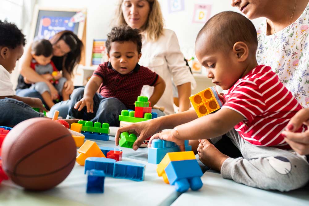 Toddlers sitting and playing with childcare professionals